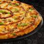 Large BBQ Chicken pizza from Debonairs Pizza placed on top of a black plate, on a black background, with shape patterns.