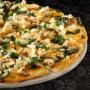 Large vegetarian Creamy Spinach & Feta pizza from Debonairs Pizza placed on top of a black plate, on a black background, with shape patterns.