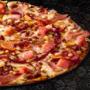 Large Something Meaty pizza from Debonairs Pizza placed on top of a black plate, on a black background, with shape patterns.
