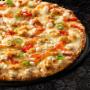 Large vegetarian Sweet Chilli pizza placed on top of a black plate, on a black background, with shape patterns.