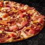 Large Something Meaty pizza from Debonairs Pizza placed on top of a black plate, on a black background, with shape patterns.