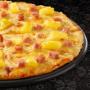Large Hawaiian pizza from Debonairs Pizza placed on top of a black plate, on a black background, with shape patterns.
