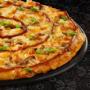 Large BBQ Chicken pizza from Debonairs Pizza placed on top of a black plate, on a black background, with shape patterns.